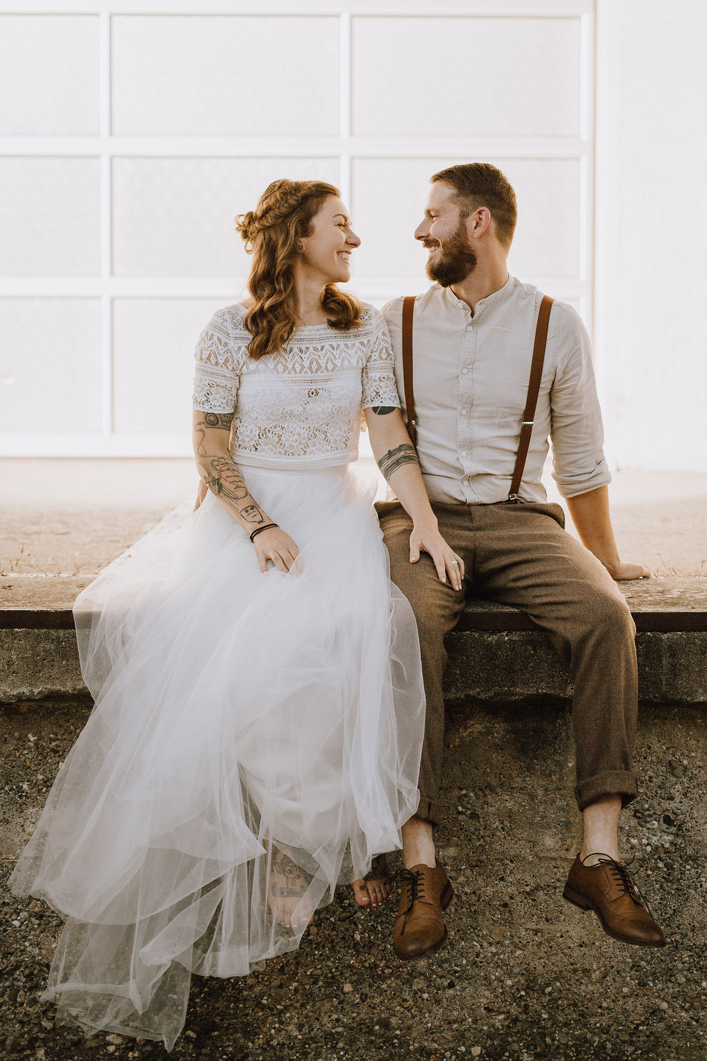 Styled Shoot, Brautpaar mit Boho Brautkleid zweiteilig, nebeneinander auf Mauer sitzend