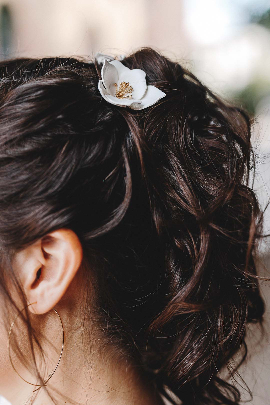 noni Brautmode, Nahaufnahme/Detailbild von blütenförmigem Haarschmuck in brünettem Haar